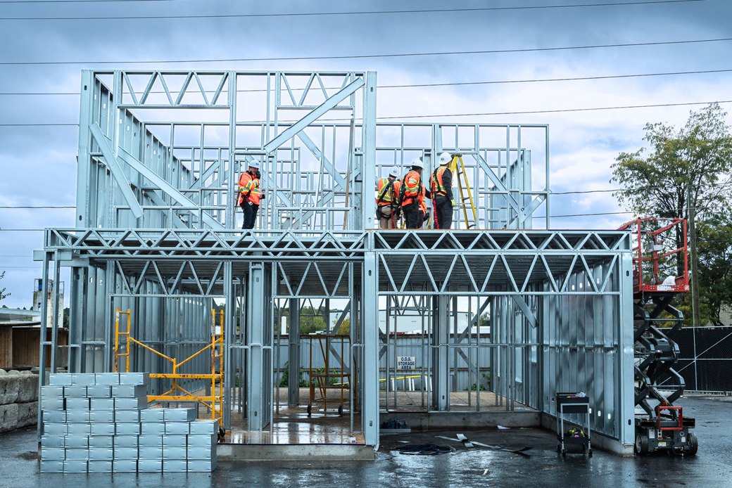 Two-storey cold-formed steel demonstration frame with workers in the EBS yard, Barrie