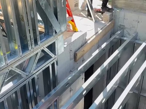 Galvanized steel wall panels and floor joists being set on a concrete foundation