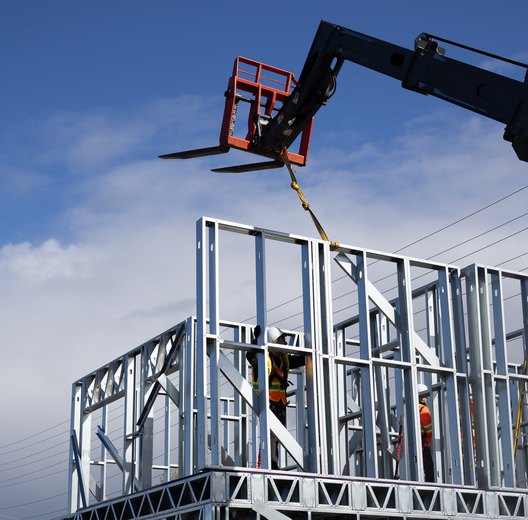 Telehandler lowering a cold-formed steel wall panel onto a frame