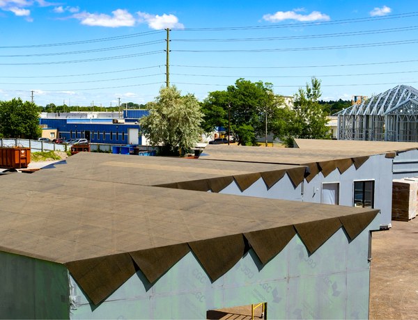 Modular classroom units with roofing under way, in the yard outside the plant