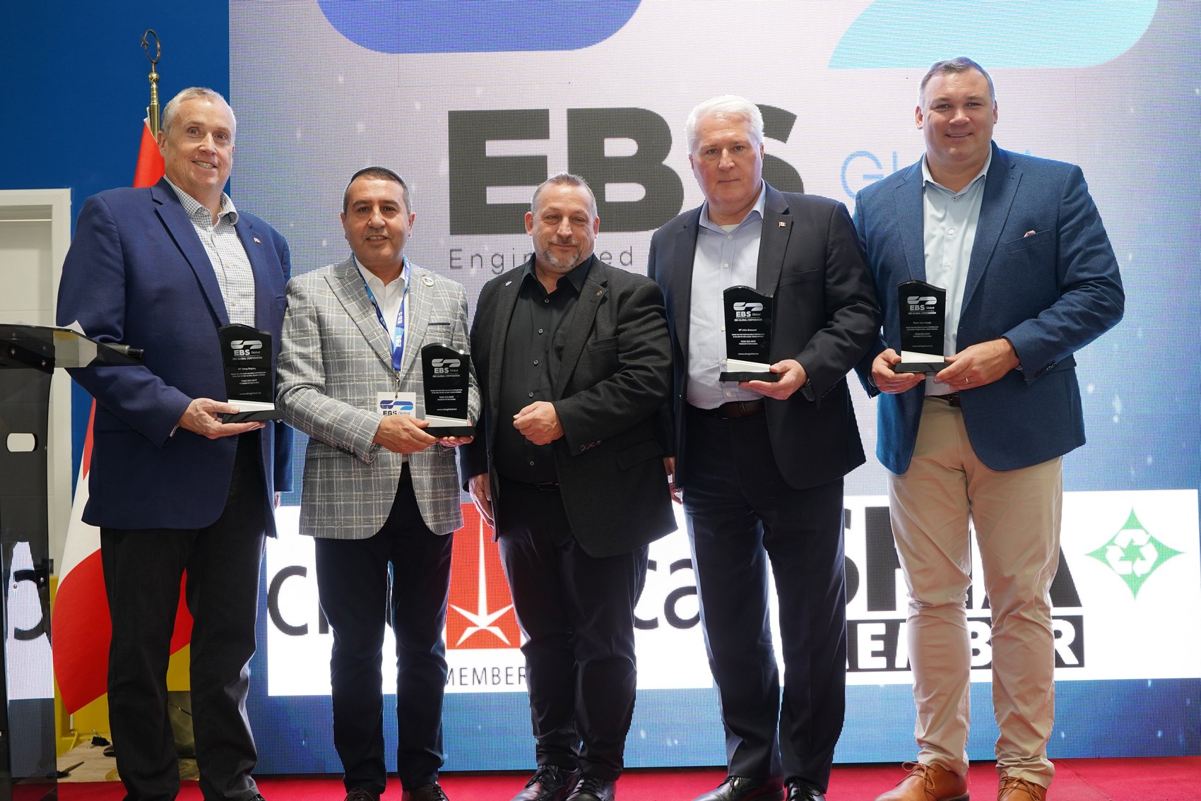 Guests holding plaques on stage at the EBS Global grand opening in Barrie