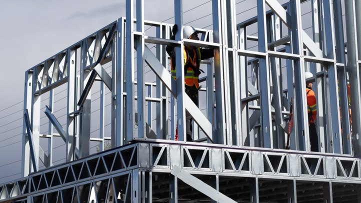 A telehandler lowering a cold-formed steel wall panel onto a two-storey frame